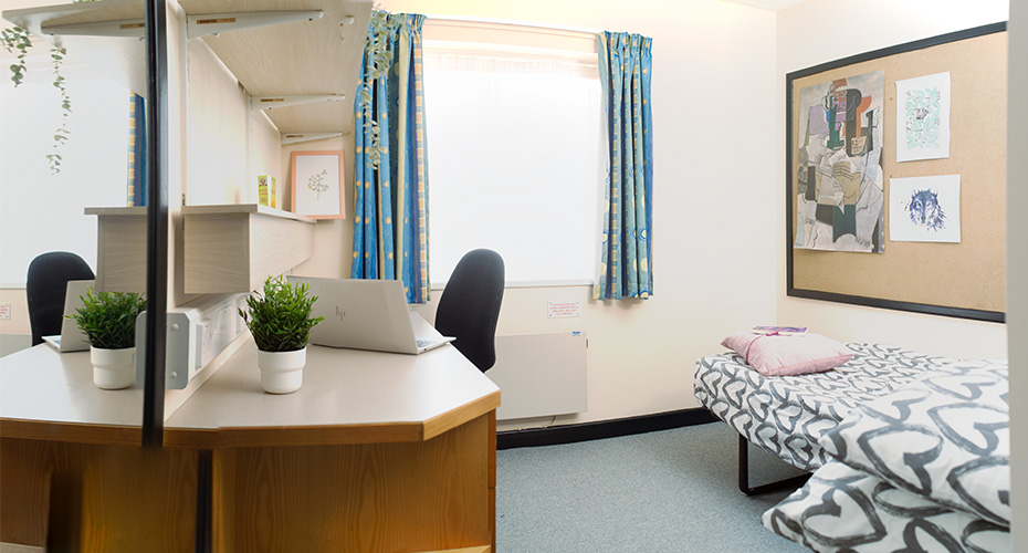 Desk with laptop and office chair, open blue curtains, single bed