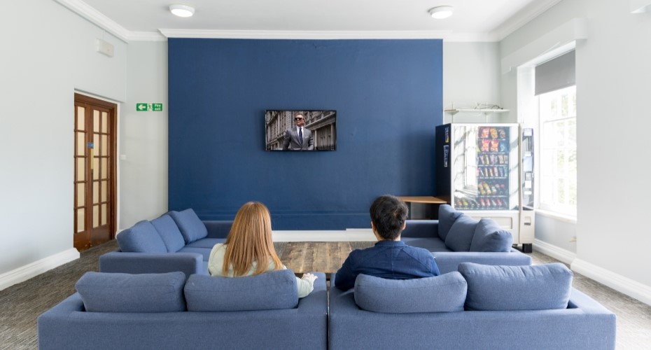 Two students sitting on blue sofas watching James Bond in Lopes Common Room