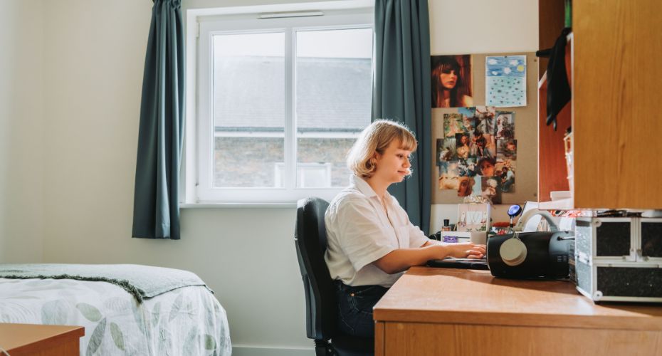 Student working on laptop on desk in bedroom