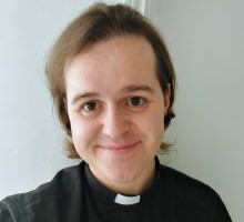A headshot of Sam Fletcher, dressed in black with a priest